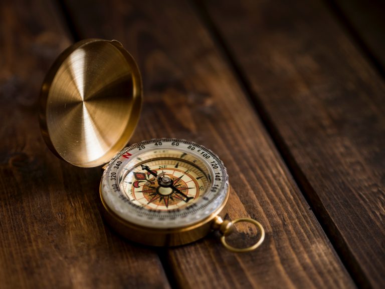 A gold compass aligned north sits on a wooden bench.
