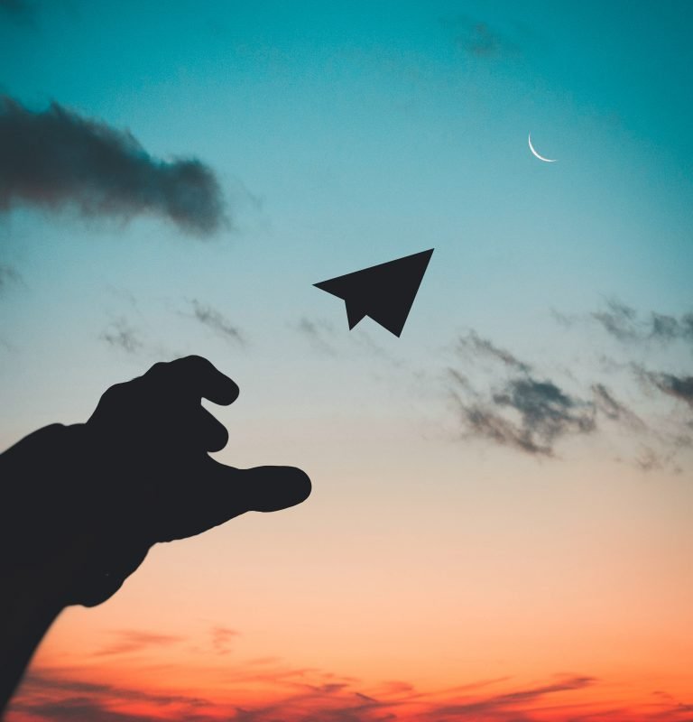 A silhouette of a hand releasing a paper plane into the sunset.