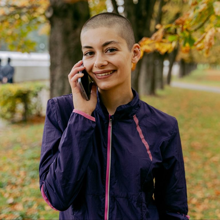 A woman with shaved hair receives a phone call while in a park